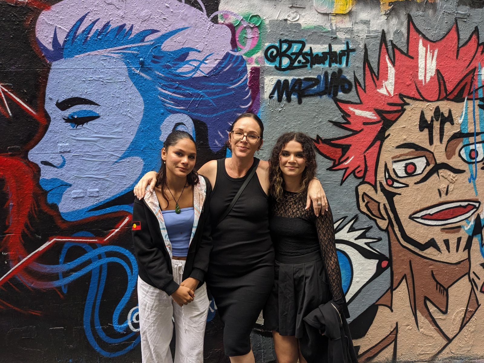 Chelsea stands in between her two daughters, in front of a graffiti wall