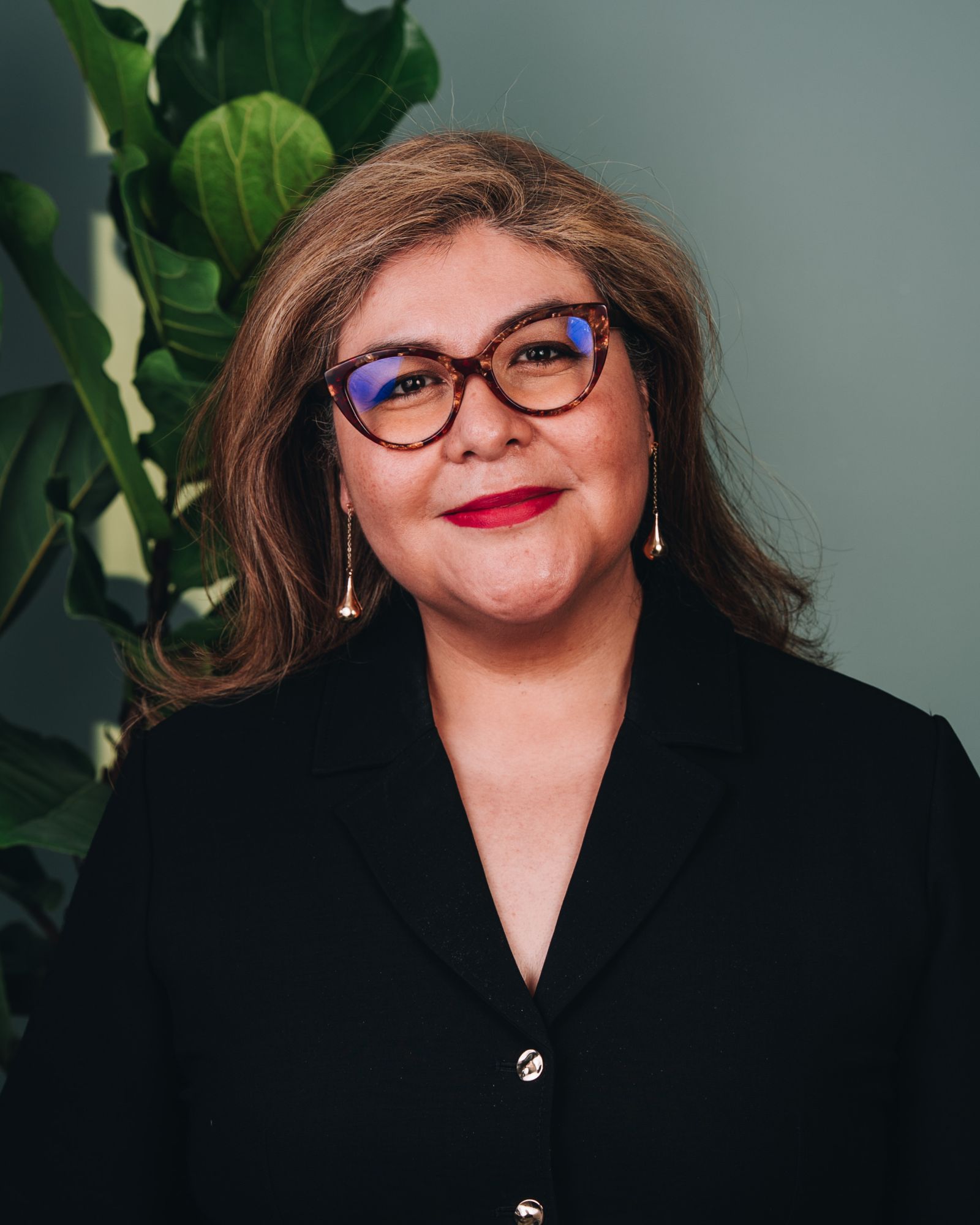 Myrna wears glasses, long earrings and a black suit jacket
