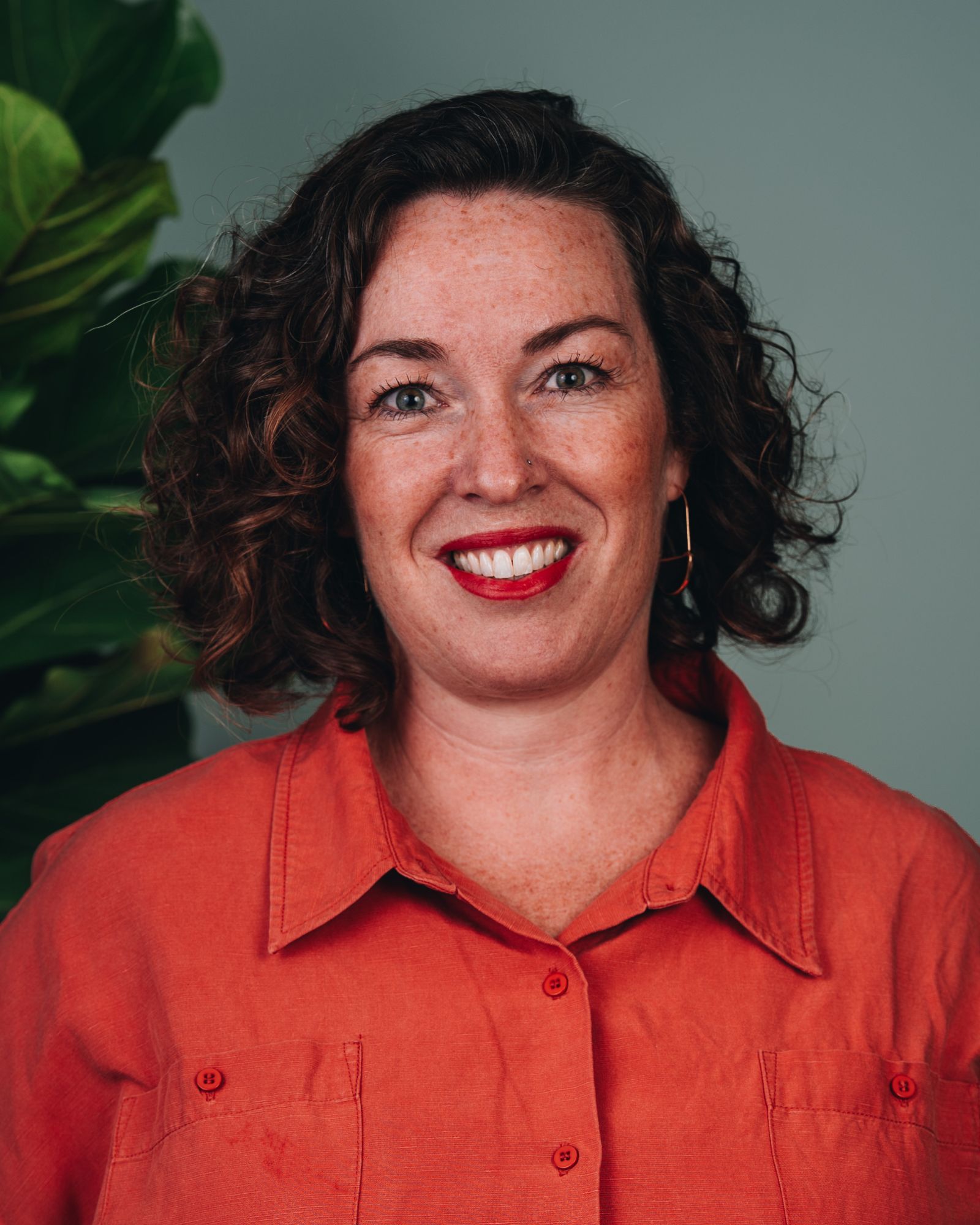 Kyle has curly hair, wears a bright orange top and red lipstick with her big smile