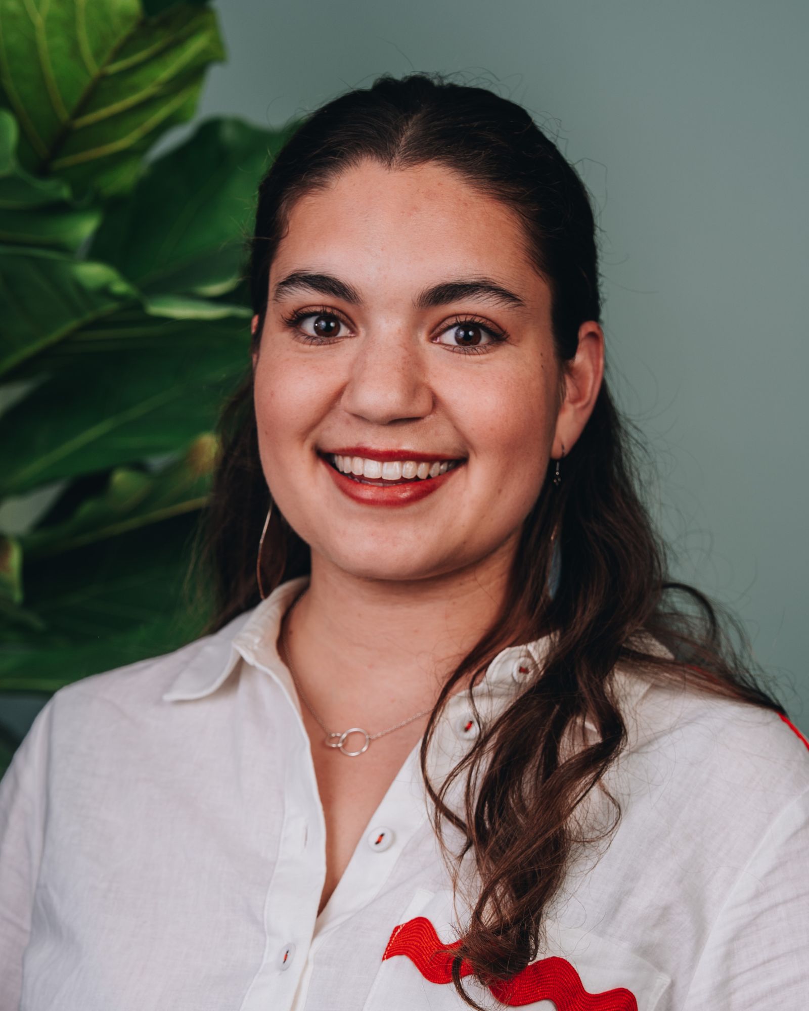 Aimee is smiling, wearing a white shirt with red detailing which matches her red lipstick