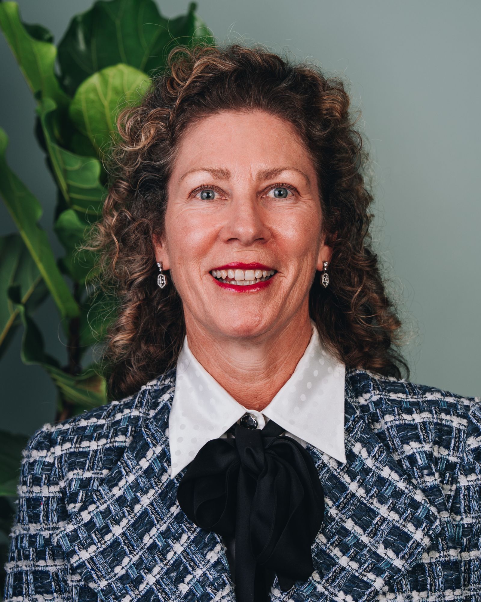 Renee wears a blue and white patterned blazer, a black bow tie and has long curly hair and a big smile