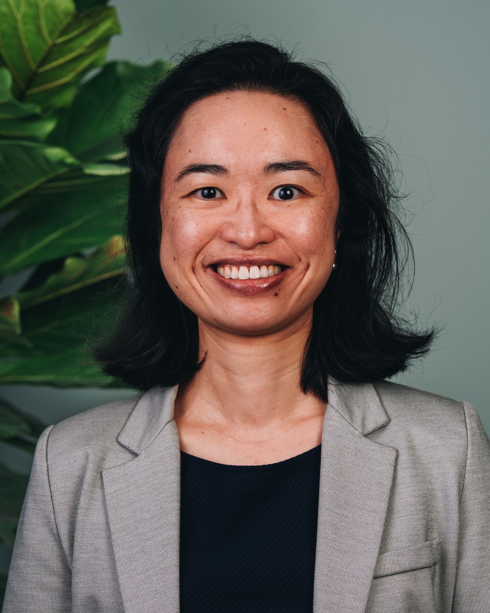 Tanya wears a beige blazer atop a black shirt, has short dark hair and a big smile