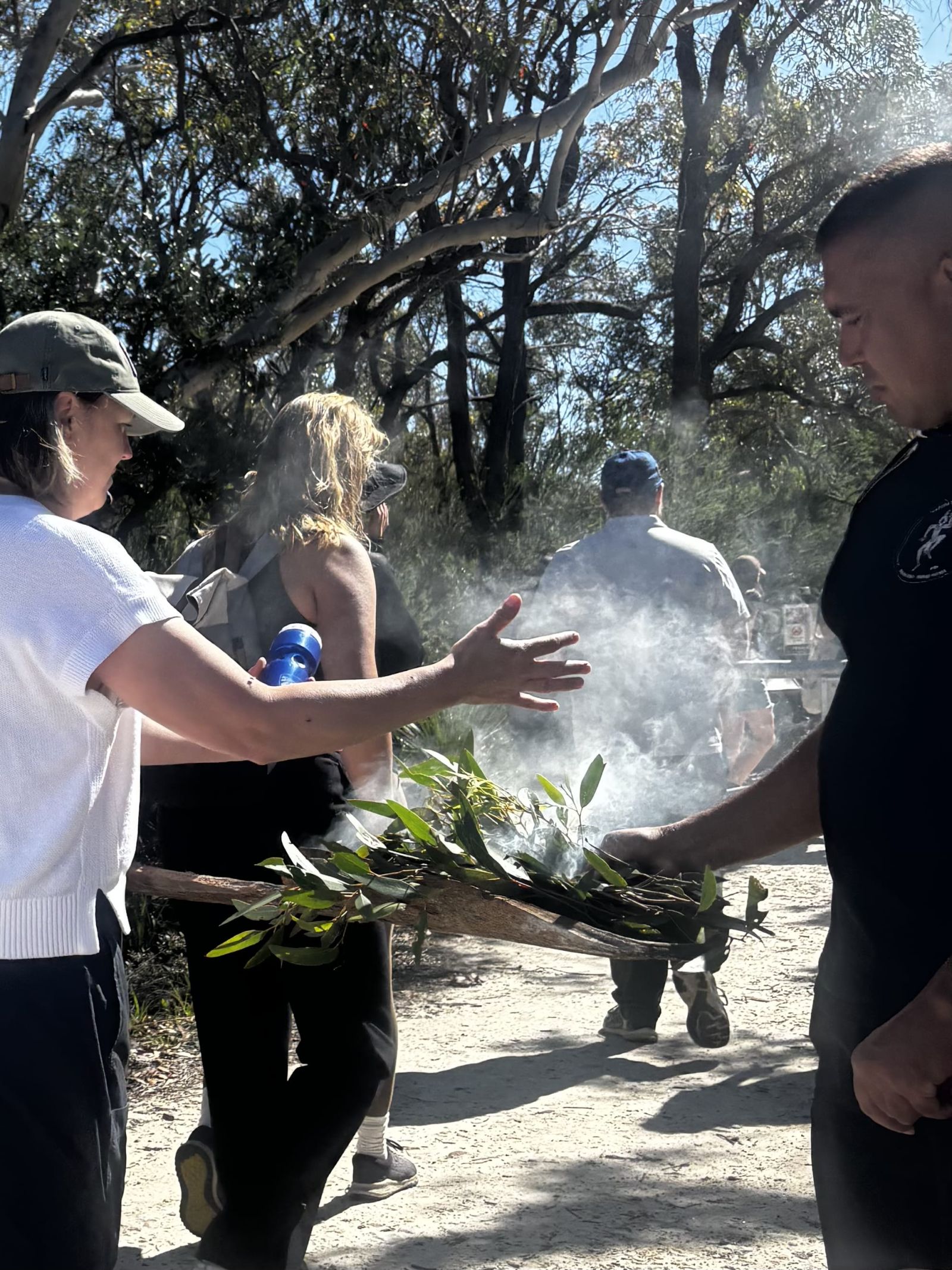 A smoking ceremony, a Sefa team member embraces the smoke coming from eucalyptus leaves
